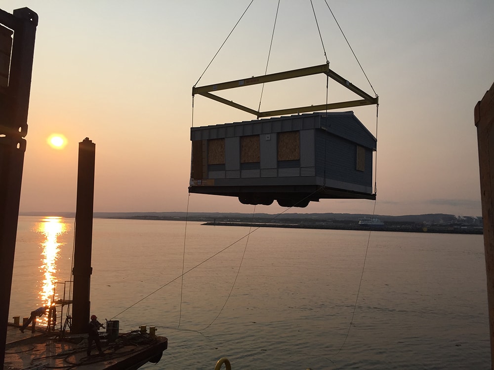 Module préfabriqué soulevé par grue au port de Matane, au coucher du soleil
